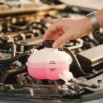 A warm, inviting close-up of a non-identifiable hand meticulously checking a car's coolant reservoir in a clean engine bay