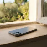 A gray smartphone rests on a stone windowsill overlooking a sunlit garden